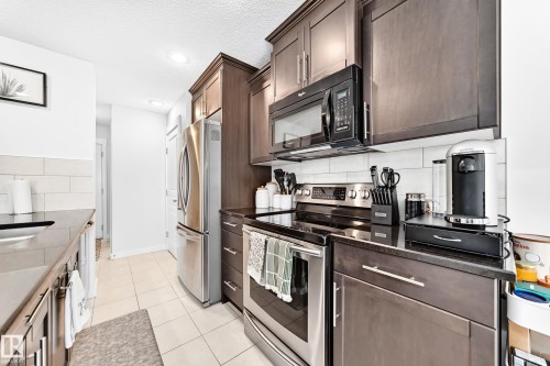 Kitchen featuring dark wood-finish cabinetry, stainless steel appliances, black countertops, a white subway tile backsplash, and recessed lighting - 16832 53 Street Nw, Edmonton, AB 