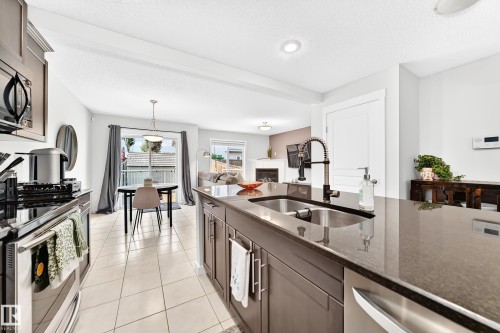 Open-concept kitchen with a large island, stainless steel appliances, dark cabinetry, and a double basin sink with a gooseneck faucet - 16832 53 Street Nw, Edmonton, AB 