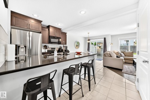 Kitchen featuring dark wood cabinetry, stainless steel appliances, a breakfast bar, and tile flooring - 16832 53 Street Nw, Edmonton, AB 