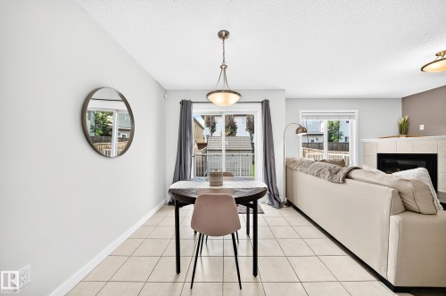 Neutral tile flooring, built-in fireplace with tile surround, glass patio door, and pendant light fixture - 16832 53 Street Nw, Edmonton, AB 
