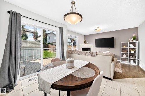 Open-concept living area with a fireplace, hard-surface flooring, and a sliding glass door leading to an outdoor deck and fenced yard - 16832 53 Street Nw, Edmonton, AB 