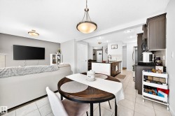 Open-concept living space featuring a dining area with a wood-finish table, a kitchen with dark cabinetry and stainless steel appliances, and tile flooring throughout - 