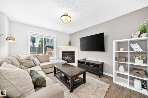 Living space featuring wood-finish flooring, a white mantel fireplace, and a large window with exterior visibility - 16832 53 Street Nw, Edmonton, AB 