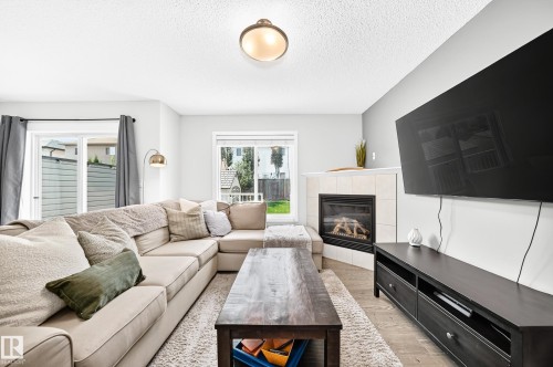 Living space featuring a corner fireplace with a tile surround, large sliding glass door, and wood-finish flooring - 16832 53 Street Nw, Edmonton, AB 