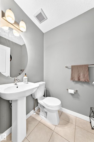 Pedestal sink with chrome faucet, round wall-mounted mirror, ceramic tile flooring, and integrated ceiling ventilation - 16832 53 Street Nw, Edmonton, AB 