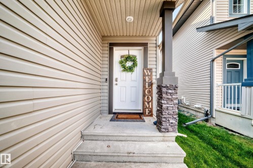 Covered front entrance with stone accent column, concrete steps, and light-colored siding - 16832 53 Street Nw, Edmonton, AB 