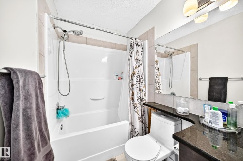 Recessed bathtub with integrated shower, wall-mounted showerhead, tiled surround, and dark granite countertop - 16832 53 Street Nw, Edmonton, AB 