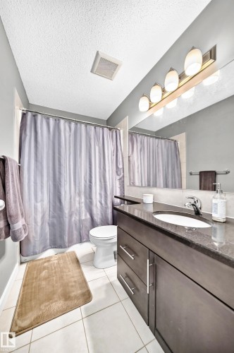 White tile flooring with a dark wood-finish vanity, integrated sink, and a large mirror - 16832 53 Street Nw, Edmonton, AB 