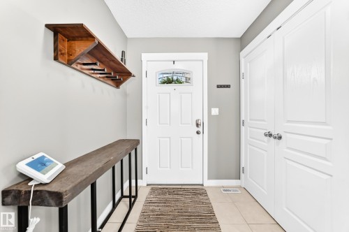 Entryway featuring a paneled door with an arched glass insert, tiled flooring, built-in shelving, and white bi-fold closet doors - 16832 53 Street Nw, Edmonton, AB 