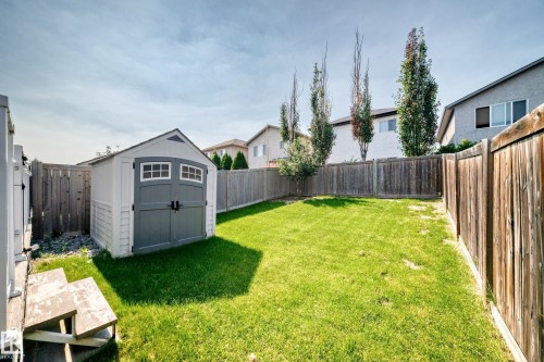 Expansive fenced backyard featuring a storage shed with double doors, established grass, and mature trees - 16832 53 Street Nw, Edmonton, AB 