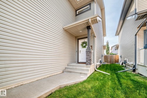 Light-toned siding exterior featuring a covered entry, stone-clad column, white front door, and concrete walkway - 16832 53 Street Nw, Edmonton, AB 
