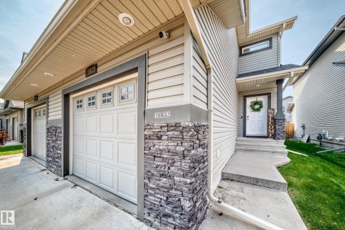 Exterior featuring horizontal siding, stacked stone accents, two attached garages with window inserts, a covered entry, and concrete pathways - 16832 53 Street Nw, Edmonton, AB 