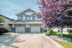 Contemporary multi-level exterior with gabled roof lines, dual attached garage doors, stone veneer accents, and a concrete driveway - 