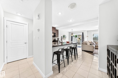 Light-toned tile flooring, white interior doors, recessed lighting, kitchen with dark cabinetry, and black countertop bar seating - 16832 53 Street Nw, Edmonton, AB 