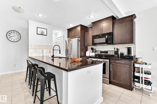 Kitchen featuring a substantial island with seating, dark wood-finish cabinetry, a white tile backsplash, stainless steel appliances, and recessed ceiling lighting - 16832 53 Street Nw, Edmonton, AB 