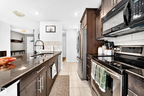 Kitchen featuring dark wood-finish cabinetry, stainless steel appliances, a black electric range, a black microwave, and tile flooring - 16832 53 Street Nw, Edmonton, AB 