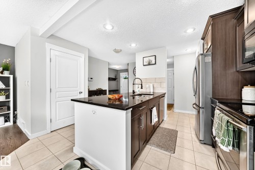Kitchen featuring dark wood-finish cabinetry, stainless steel appliances, a center island with a dark countertop, recessed lighting, and tiled flooring - 16832 53 Street Nw, Edmonton, AB 