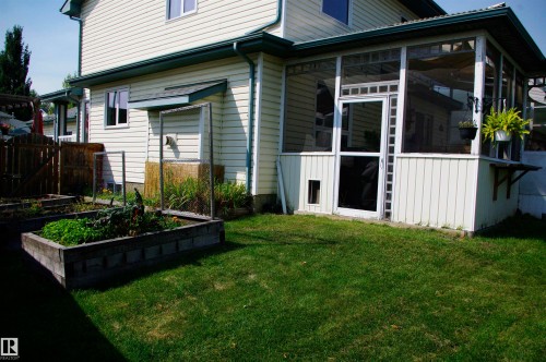 Spacious backyard featuring a manicured lawn, screened-in porch with white paneling, and an elevated garden bed - 25 Hasen Close, St. Albert, AB 