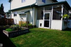Spacious backyard featuring a manicured lawn, screened-in porch with white paneling, and an elevated garden bed - 