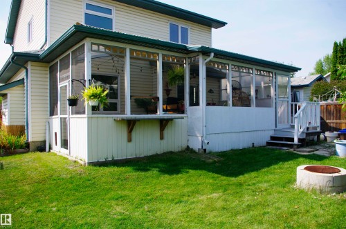 Expansive screened-in porch with a corrugated metal roof, white siding exterior, and exterior stairs leading to a grassy yard - 25 Hasen Close, St. Albert, AB 