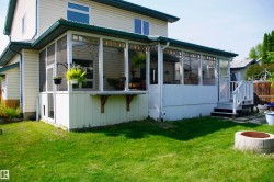 Expansive screened-in porch with a corrugated metal roof, white siding exterior, and exterior stairs leading to a grassy yard - 