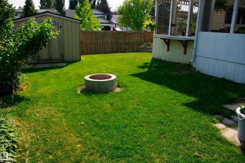 Manicured lawn with a fire pit, privacy fencing, and a detached storage shed - 25 Hasen Close, St. Albert, AB 