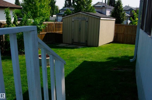 Expansive backyard featuring a shed with double doors, wood fencing, and a white wood railing - 25 Hasen Close, St. Albert, AB 