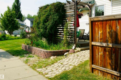 Expansive front yard featuring a manicured lawn, brick-block retaining wall, and a stone paver pathway - 25 Hasen Close, St. Albert, AB 