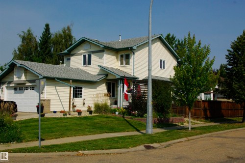 Light-toned siding exterior with a two-car garage, gray shingled roof, and a privacy fence bordering the property - 25 Hasen Close, St. Albert, AB 