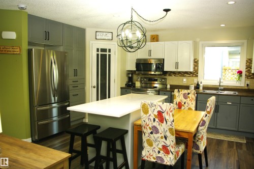 Kitchen featuring a center island with bar seating, stainless steel appliances, wood-finish flooring, and two-tone cabinetry - 25 Hasen Close, St. Albert, AB 