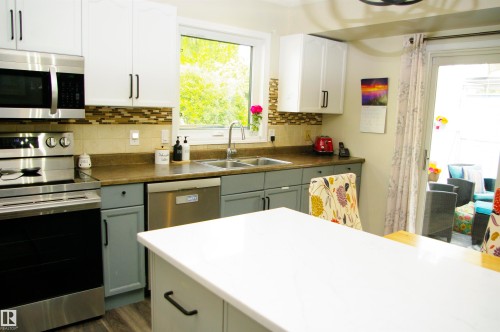 White upper cabinetry and gray lower cabinetry, stainless steel appliances, mosaic tile backsplash, wood-finish flooring, and a white countertop island - 25 Hasen Close, St. Albert, AB 