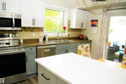 White upper cabinetry and gray lower cabinetry, stainless steel appliances, mosaic tile backsplash, wood-finish flooring, and a white countertop island - 