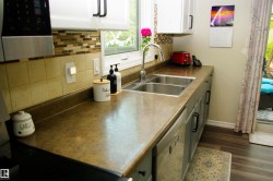 Kitchen featuring a double basin stainless steel sink, wood-finish flooring, and light-colored cabinetry with dark hardware - 