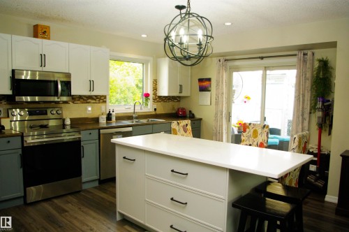 Kitchen featuring stainless steel appliances, wood-finish flooring, a central island with a white countertop, and a sliding glass door - 25 Hasen Close, St. Albert, AB 