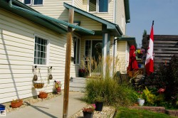 Light-colored vinyl siding exterior, concrete walkway, porch with overhead covering, partial wood fencing, and mature landscaping - 