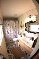 Patterned floor tile, white subway tile shower surround, single vanity with wood-finish cabinetry, and a black ornamental framed mirror - 