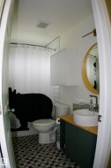 Patterned floor tile, vessel sink, wood-finish countertop, round wall mirror, and white wall-mounted cabinetry - 
