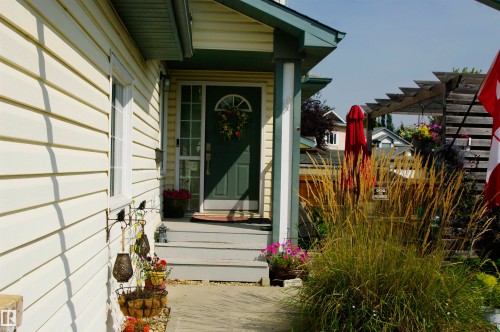 Front entry with a dark-paneled door, decorative screen door, and covered porch - 25 Hasen Close, St. Albert, AB 
