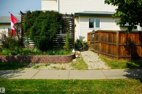Siding exterior with a wood privacy fence, brick-finish retaining wall, and established landscaping - 25 Hasen Close, St. Albert, AB 