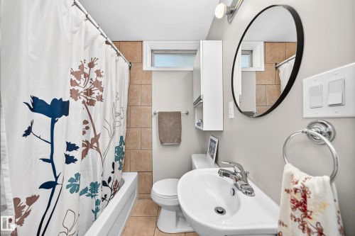 Bathtub and shower combination with tiled surround, white vanity with integrated sink, contemporary round mirror, and wall-mounted storage cabinet - 3 Grantham Place, St. Albert, AB 