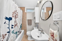 Bathtub and shower combination with tiled surround, white vanity with integrated sink, contemporary round mirror, and wall-mounted storage cabinet - 