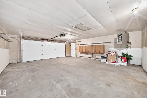 Spacious garage with concrete flooring, automatic garage door, wall-mounted cabinetry, and exposed ceiling light fixtures - 3 Grantham Place, St. Albert, AB 