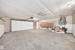Spacious garage with concrete flooring, automatic garage door, wall-mounted cabinetry, and exposed ceiling light fixtures - 