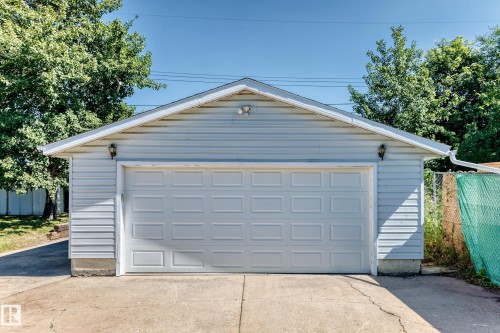 Detached garage with horizontal siding, a paneled garage door, dual exterior wall sconces, and a concrete driveway - 3 Grantham Place, St. Albert, AB 