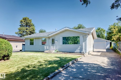 Exterior featuring light-colored siding, a front porch with railing, a paved driveway, a detached garage, and a manicured lawn - 3 Grantham Place, St. Albert, AB 