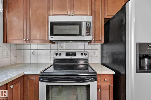 Wood-finish cabinetry, light-toned countertops, tile backsplash with accent inserts, stainless steel range, and an over-the-range microwave - 16016 78A Avenue Nw, Edmonton, AB 