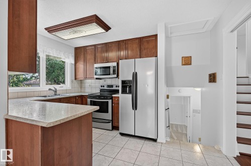 Kitchen featuring wood-finish cabinetry, stainless steel appliances, and a tiled backsplash - 16016 78A Avenue Nw, Edmonton, AB 