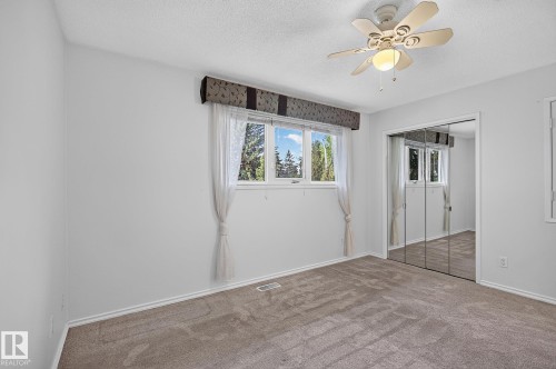 Ceiling fan with integrated lighting, window with exterior scenery, mirrored closet doors, and neutral carpeting - 16016 78A Avenue Nw, Edmonton, AB 