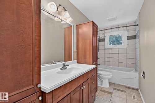 Wood-finish cabinetry and storage tower, integrated vanity sink, tiled tub surround with accent band, and tile flooring - 16016 78A Avenue Nw, Edmonton, AB 