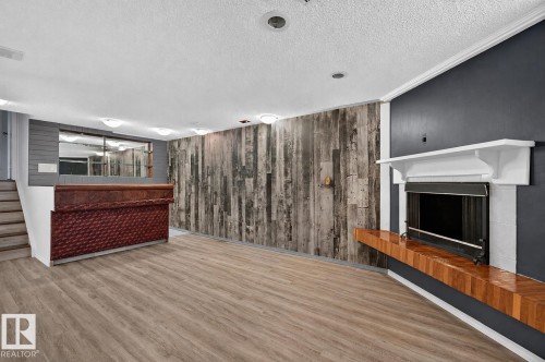 Wood-finish flooring, accent wall with varied wood paneling, built-in bar, wood mantel with integrated shelving, and white fireplace surround - 16016 78A Avenue Nw, Edmonton, AB 